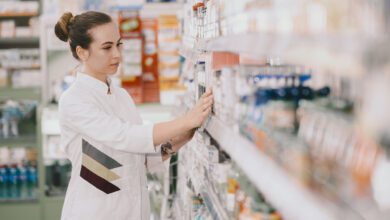 medicine pharmaceutics health care and people concept female pharmacist taking medications from the shelf