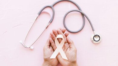 white awareness ribbon in two hands with stethoscope on pink background